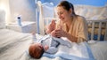 Portrait of smiling young mother smiling at her little baby son lying on bed and holding his little feet. Happy Royalty Free Stock Photo