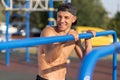 Portrait of smiling young muscular male doing pull ups exercises on horizontal bar outdoors. Happy athletic runner training hard Royalty Free Stock Photo