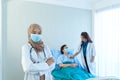 Portrait of smiling young muslim female doctor arms crossed stand in hospital with medical team working on the background Royalty Free Stock Photo