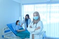 Portrait of smiling young muslim female doctor arms crossed stand in hospital with medical team working on the background Royalty Free Stock Photo