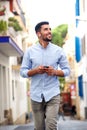 Smiling young North African man walking in the street with cellphone and headphones