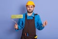 Portrait of smiling young painter with paint roller in hands, looks happy, likes his work, being ready to paint walls, keeps hands Royalty Free Stock Photo