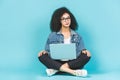 Portrait of smiling young afro american woman using laptop while sitting on a floor with legs crossed isolated over blue Royalty Free Stock Photo