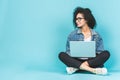 Portrait of smiling young afro american woman using laptop while sitting on a floor with legs crossed isolated over blue Royalty Free Stock Photo
