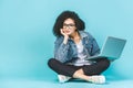 Portrait of smiling young afro american woman using laptop while sitting on a floor with legs crossed isolated over blue Royalty Free Stock Photo