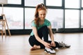 Portrait of smiling young sporty woman tying shoe laces on floor preparing for workout at gym. Front view of athletic Royalty Free Stock Photo