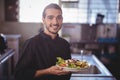 Portrait of smiling young waiter holding salad plate at commercial kitchen