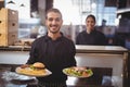 Portrait of smiling young waiter serving food while standing against waitress Royalty Free Stock Photo