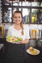 Portrait of smiling young waitress holding fresh Greek salad plate Royalty Free Stock Photo