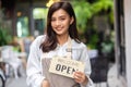 Portrait of a smiling young woman in apron holding open sign board while standing at the cafe. The coffee shop is raising the sign Royalty Free Stock Photo