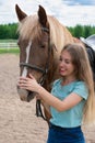 Portrait of smiling young woman with blond long hair is caressing brown horse snoot with big nostrils. Horseback riding hobby, vac Royalty Free Stock Photo