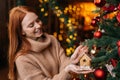 Portrait of smiling young woman decorating Christmas tree beautiful toy at cozy living room. Royalty Free Stock Photo