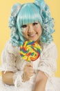 Portrait of smiling young woman dressed as a doll holding lollipop over yellow background