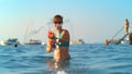 PORTRAIT: Smiling young woman enjoying her summer vacation shoots a water gun. Royalty Free Stock Photo