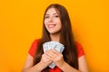 Portrait of a smiling young woman holding a bunch of money banknotes in hands isolated on a yellow background. Royalty Free Stock Photo