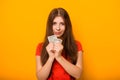 Portrait of a smiling young woman holding a bunch of money banknotes in hands isolated on a yellow background. Royalty Free Stock Photo