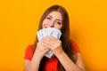 Portrait of a smiling young woman holding a bunch of money banknotes in hands  on a yellow background. Royalty Free Stock Photo