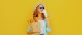 Portrait smiling young woman holding grocery shopping paper bag with long white bread baguette and coffee cup on a yellow Royalty Free Stock Photo