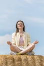 Portrait of smiling young woman meditating sitting in the hay against blue sky. Unity with nature Royalty Free Stock Photo