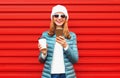 Portrait smiling young woman with phone and cup of coffee wearing a jacket and white hat on red background Royalty Free Stock Photo