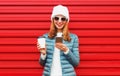 Portrait smiling young woman with phone and cup of coffee wearing a jacket and white hat on red background Royalty Free Stock Photo