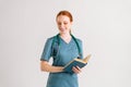 Portrait of smiling young woman physicianin green uniform with stethoscope holding medical book standing and looking Royalty Free Stock Photo