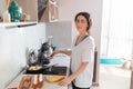 Portrait of smiling young woman is preparing breakfast in the kitchen, frying eggs. Indoor. Homemade food concept