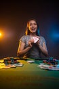 Portrait of smiling young woman siting at the table in casino and shows her lucky cards. Happy player on smoky background with Royalty Free Stock Photo