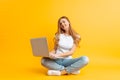 Portrait of a smiling young woman , sitting cross-legged using a laptop, on a yellow background Royalty Free Stock Photo