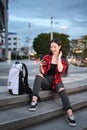 Smiling young woman sitting on stairs in the city at night and using smart phone. Royalty Free Stock Photo