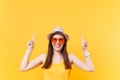 Portrait of smiling young woman in straw summer hat, orange glasses pointing index fingers up on copy space isolated on