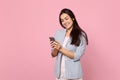 Portrait of smiling young woman in striped jacket using mobile phone, typing sms message isolated on pink pastel