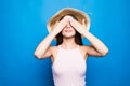 Portrait of a smiling young woman in summer hat covering eyes with her arms isolated over blue background Royalty Free Stock Photo