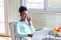 Portrait of a smiling young woman talking on mobile phone and working on laptop at home. Attractive young African woman working on Royalty Free Stock Photo