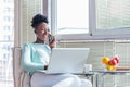 Portrait of a smiling young woman talking on mobile phone and working on laptop at home. Attractive young African woman working on Royalty Free Stock Photo