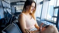 Portrait of smiling young woman waiting for flight in airport and browsing social media on smartphone Royalty Free Stock Photo