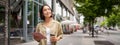 Portrait of smiling young woman walking in city with tablet, drinking takeaway coffee, going down the street with happy Royalty Free Stock Photo