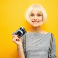 Portrait of a smilling girl with a camera in hand on a yellow background. Isolated studio. blonde wig Royalty Free Stock Photo