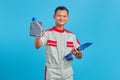 Portrait of smilling young asian mechanic holding clipboard and showing plastic bottle of engine oil in hand over blue background