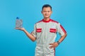 Portrait of smilling young asian mechanic showing engine oil plastic bottle in palm over blue background