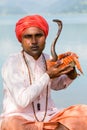 Portrait snake charmer adult man in turban and cobra sitting near the lake. Pokhara, Nepal