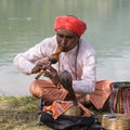 Portrait snake charmer adult man in turban and cobra sitting near the lake. Pokhara, Nepal