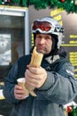 Portrait of a snowboarder with a hot dog. A middle-aged Caucasian ethnicity man in a safety helmet on a ski slope is resting Royalty Free Stock Photo