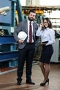 Portrait of a solid businessman with his secretary holding white hard hat, talking about factory financial report Royalty Free Stock Photo