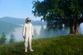 Portrait of a spaceman wearing white space suit and a helmet standing on a green meadow on a hill in the mountains