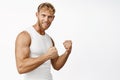 Portrait of sportsman flexing biceps, showing strong arms, masculine body during workout, standing over white background