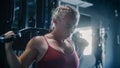 A Portrait Of Sporty Blond Woman Working out using Lat Pull Down Machine in a Dark Gym. A Resilient
