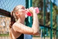 .Portrait of sporty young woman drinking cool water from bottle on summer sports field. Healthy lifestyle concept Royalty Free Stock Photo