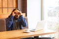 Portrait of spying handsome young adult man freelancer in casual style sitting in cafe with laptop, holding hand near eyes, making Royalty Free Stock Photo