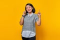 Portrait of ssmiling young Asian woman holding smartphone with an idea or question pointing finger on yellow background Royalty Free Stock Photo